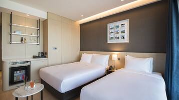 Habitación de hotel con dos camas, una mesita con una bebida, un minibar y una exhibición de fotos en la pared.