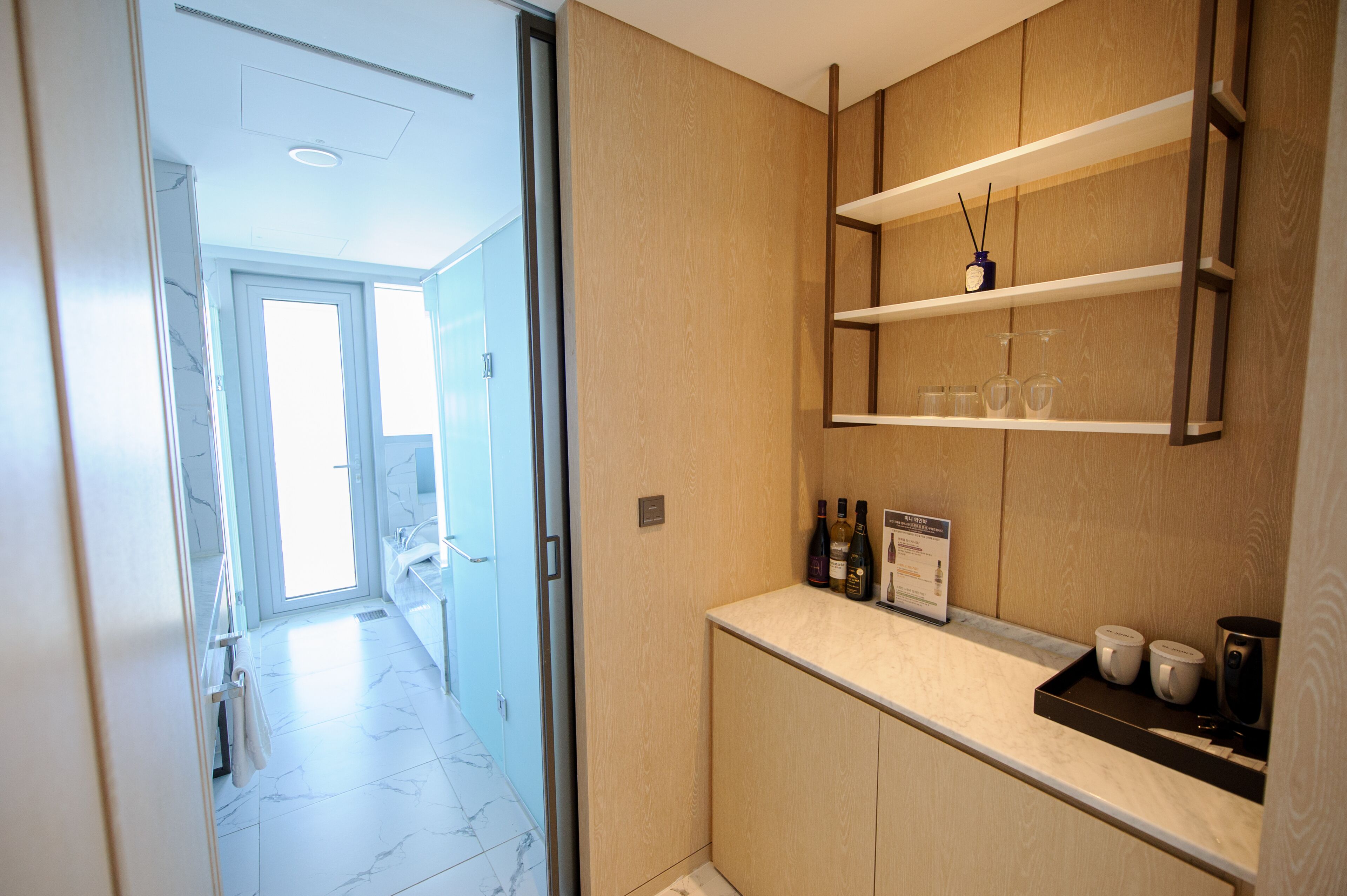 Een moderne badkamer met een marmeren vloer, een houten wastafelmeubel en een plank met flessen en glazen.
