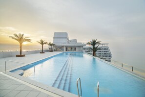 A swimming pool with a modern building in the background, surrounded by palm trees.