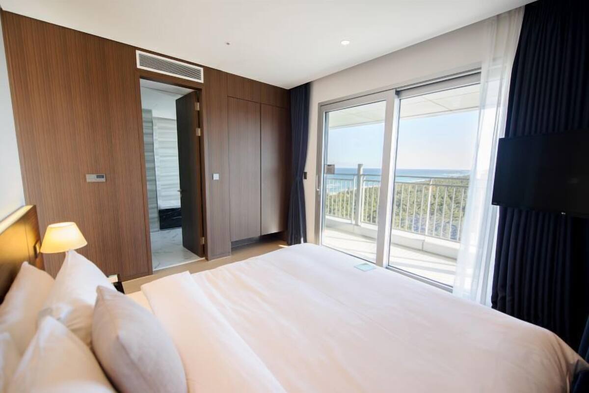 A hotel room with a large bed, a sliding door leading to a balcony, and a view of the sea.