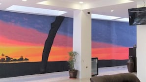 Un vestíbulo con un mural de atardecer, una planta en maceta y un sofá de cuero marrón.