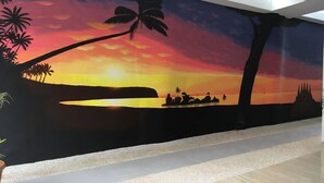 Un mural que muestra un atardecer sobre el agua, con palmeras y un velero.