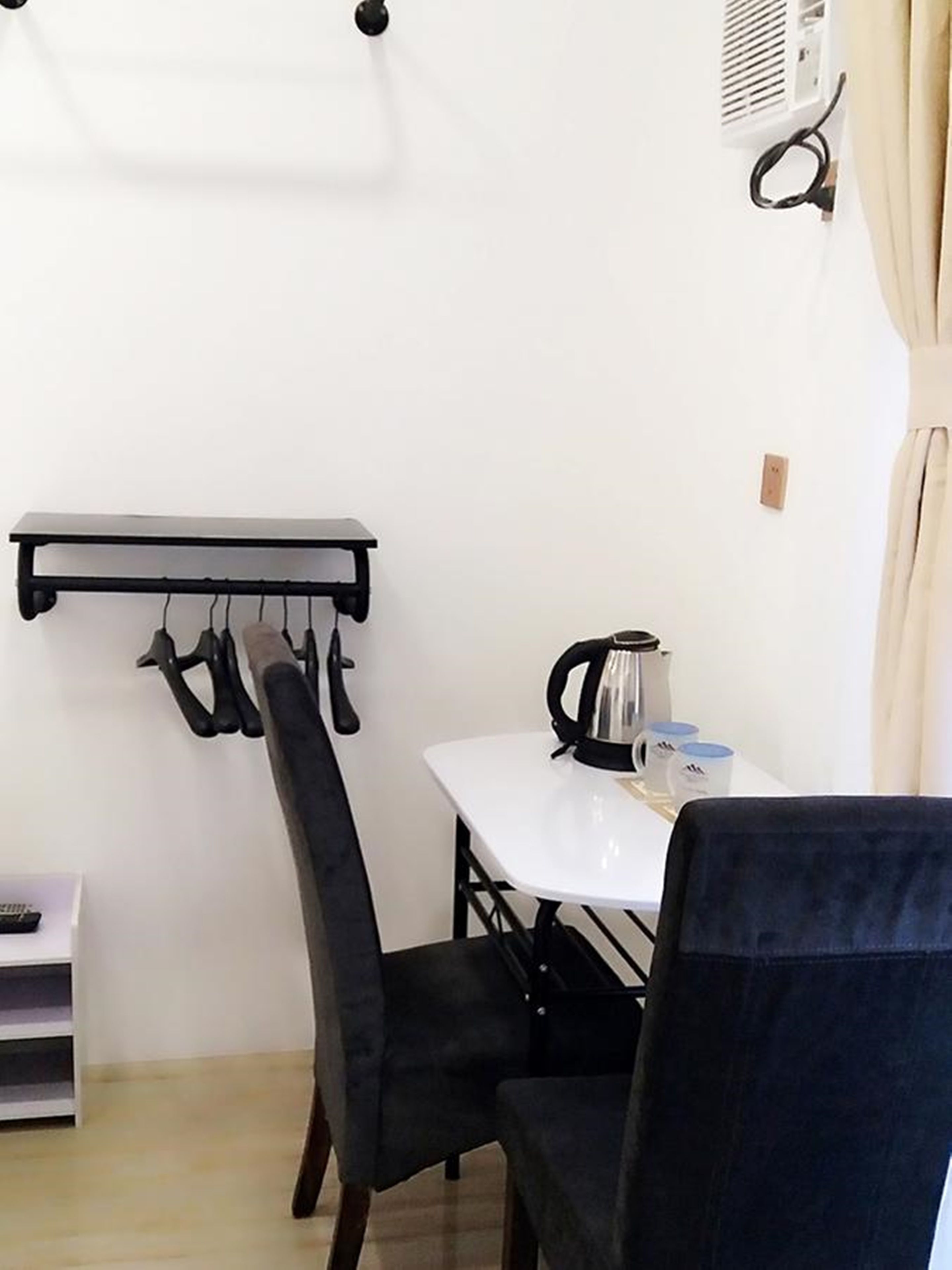 A compact room with a white table, a black chair, a hook for hanging items, and a kettle on the table.