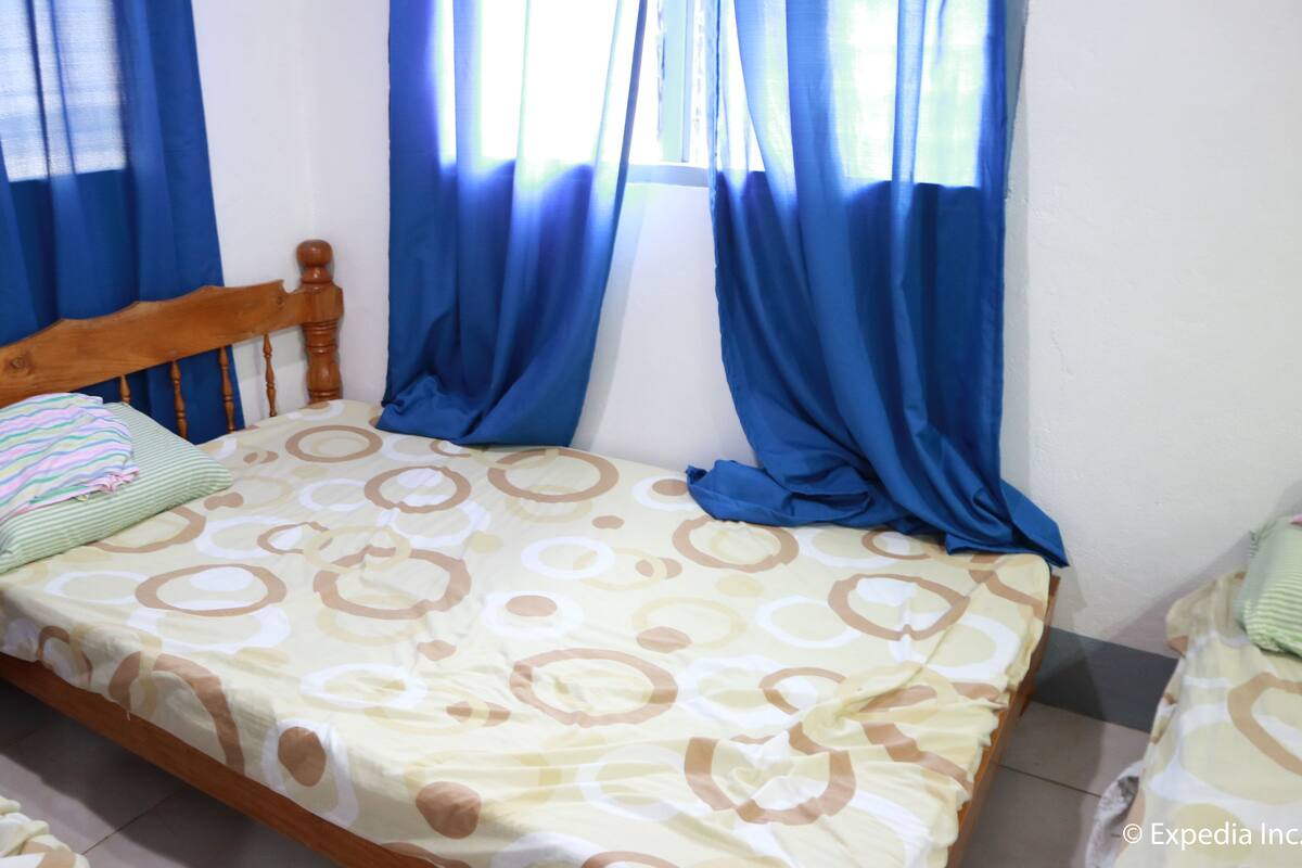 Una cama individual con cabecera de madera, una colcha estampada y cortinas azules.