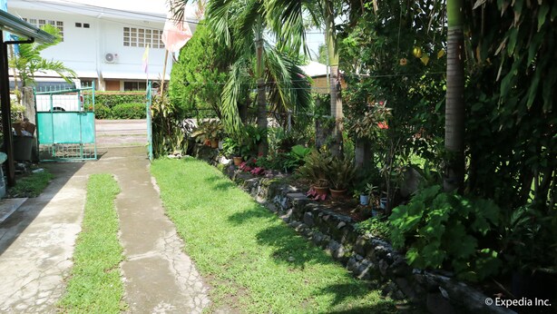 A pathway leading to a white building with a flag, surrounded by lush greenery and potted plants. - Tabada Homestay (Mambajao)