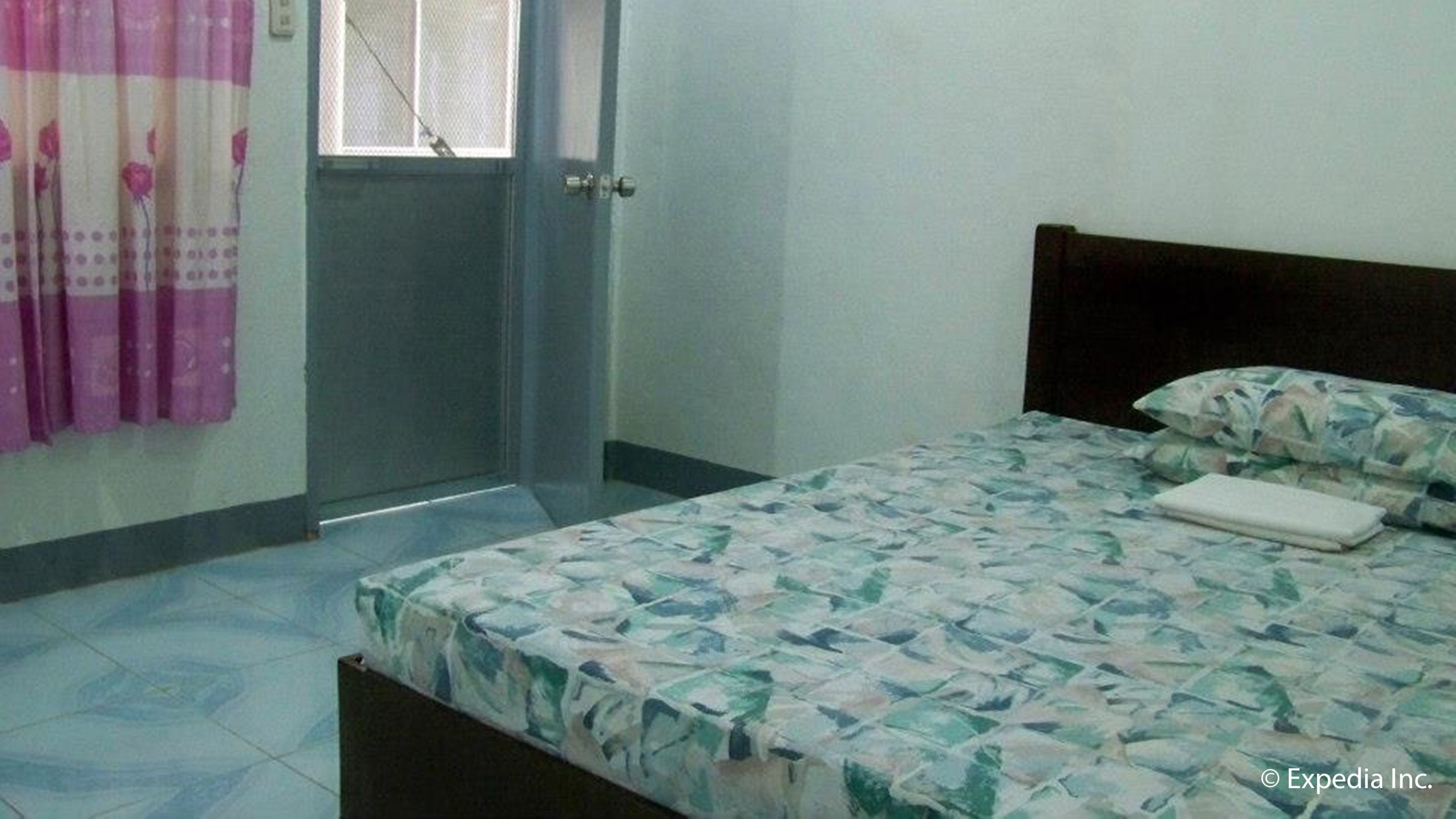 A bedroom with a bed, a window with a curtain, and a door.