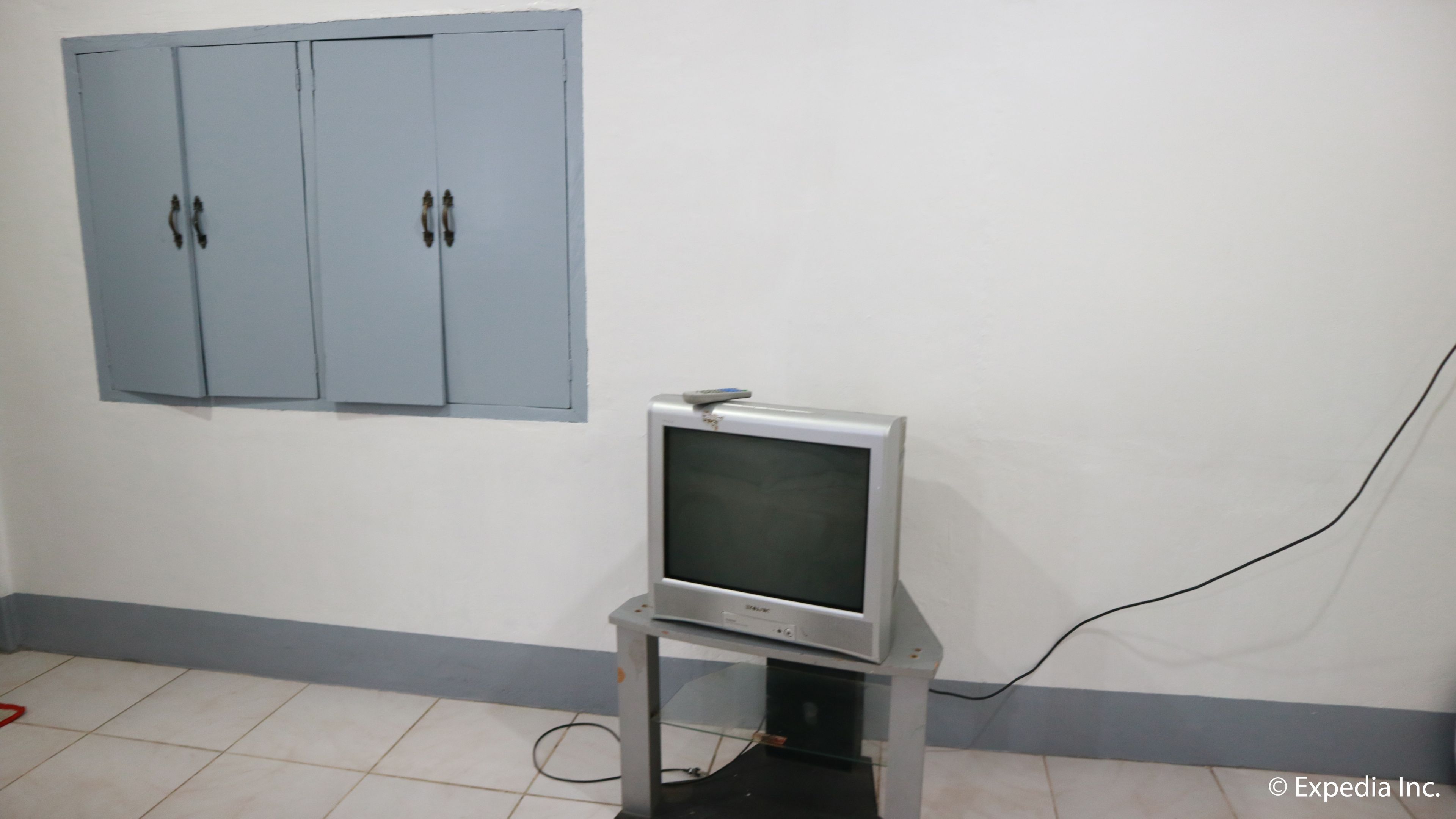 Quarto com televisão em um suporte, um armário azul e uma tomada visível.