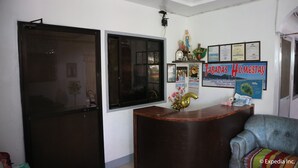 A reception area with a wooden desk, a blue armchair, and a wall with various informational posters and a religious statue. - Tabada Homestay (Mambajao)
