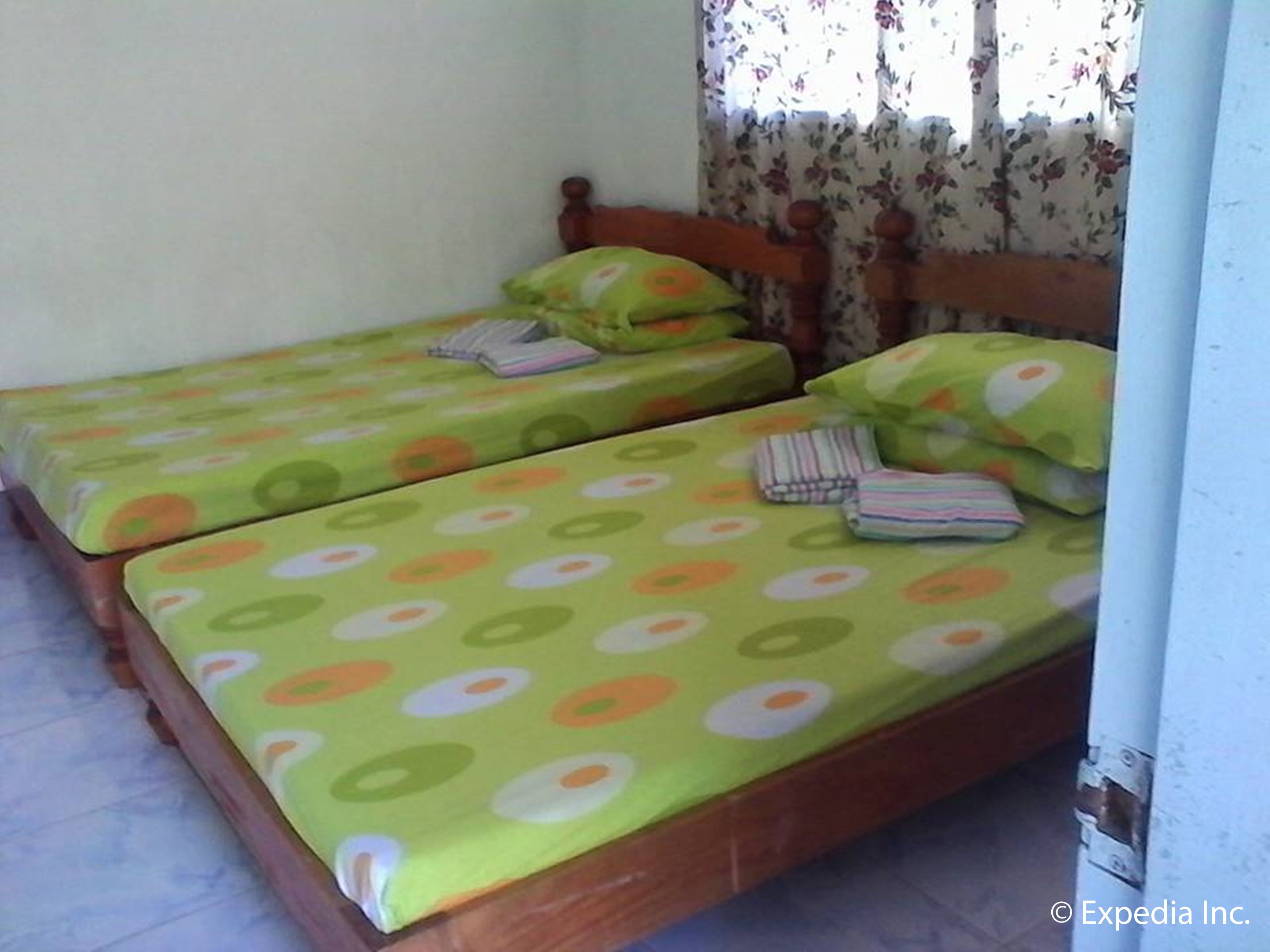 Two single beds with green and orange circular patterns, wooden headboards, and floral curtains.