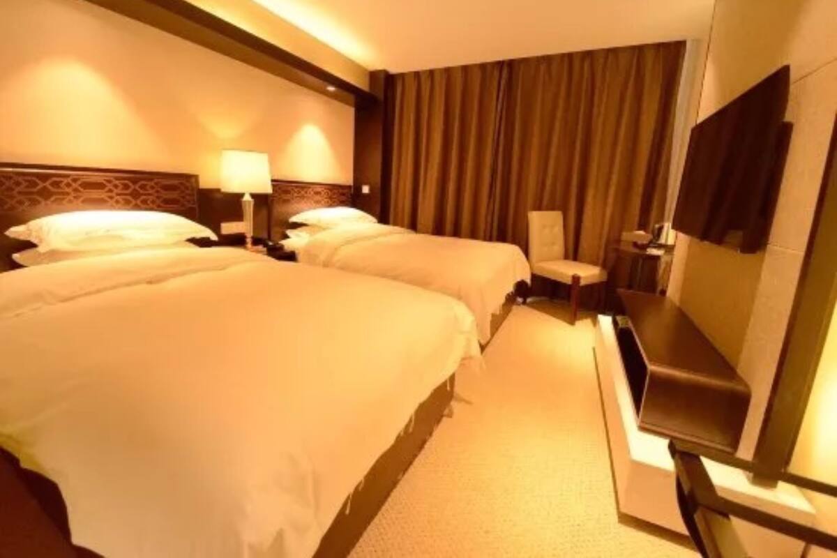 A hotel room with two beds, a desk, a chair, and a TV.