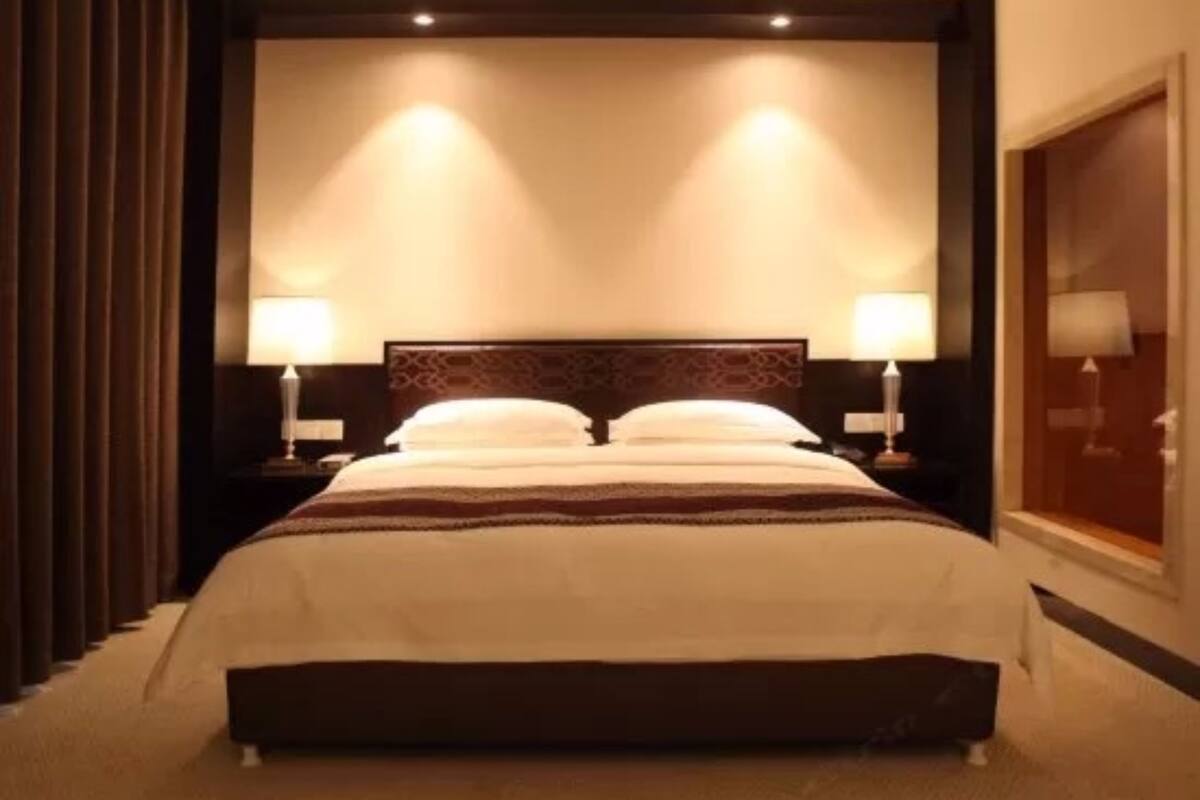 A hotel room with a large bed, two bedside lamps, and a headboard with a decorative pattern.