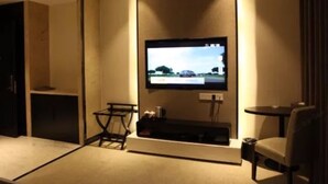 A hotel room with a flat-screen TV mounted on the wall, a small table with a chair, and a carpeted floor. - Harbin Yuxuan Hotel (Harbin)