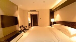 A hotel room with a large bed, a flat-screen TV mounted on the wall, a desk with a chair, and a door leading to a bathroom. - Harbin Yuxuan Hotel (Harbin)
