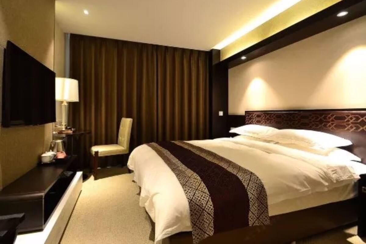 A hotel room with a large bed, a flat-screen TV, a desk with a lamp, and a chair.