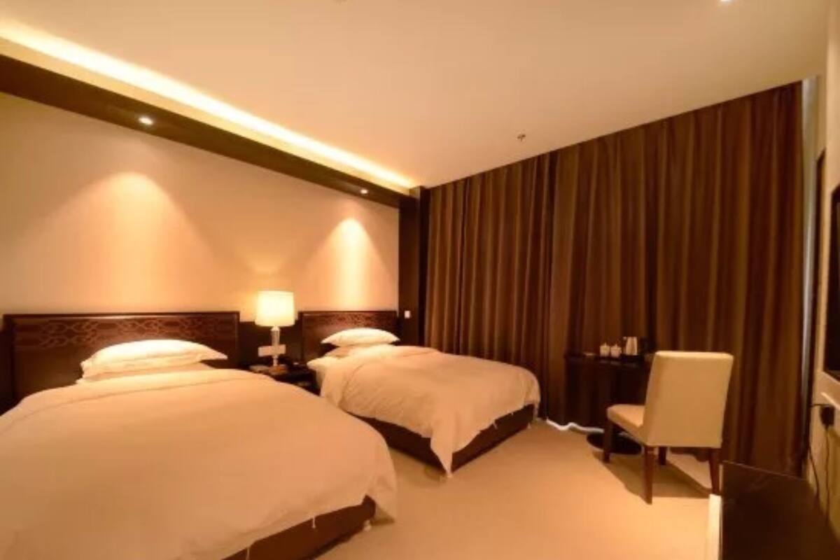 A hotel room with two beds, a nightstand with a lamp, a chair, and a large window with curtains.