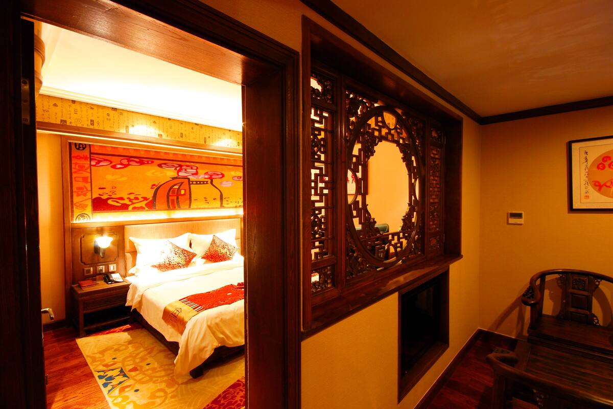 Quarto de hotel com uma cama, mesa de cabeceira e um painel decorativo de madeira.