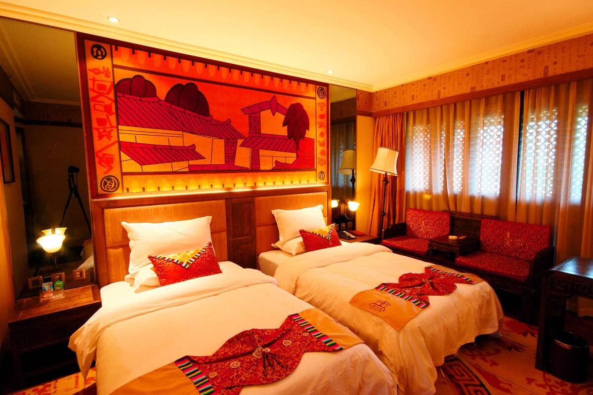 Quarto de hotel com duas camas, um sofá e um painel decorativo grande na parede.