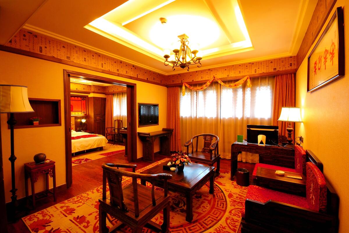 Quarto de hotel com decoração tradicional, apresentando uma cama, uma escrivaninha, uma cadeira, uma televisão e um candelabro.