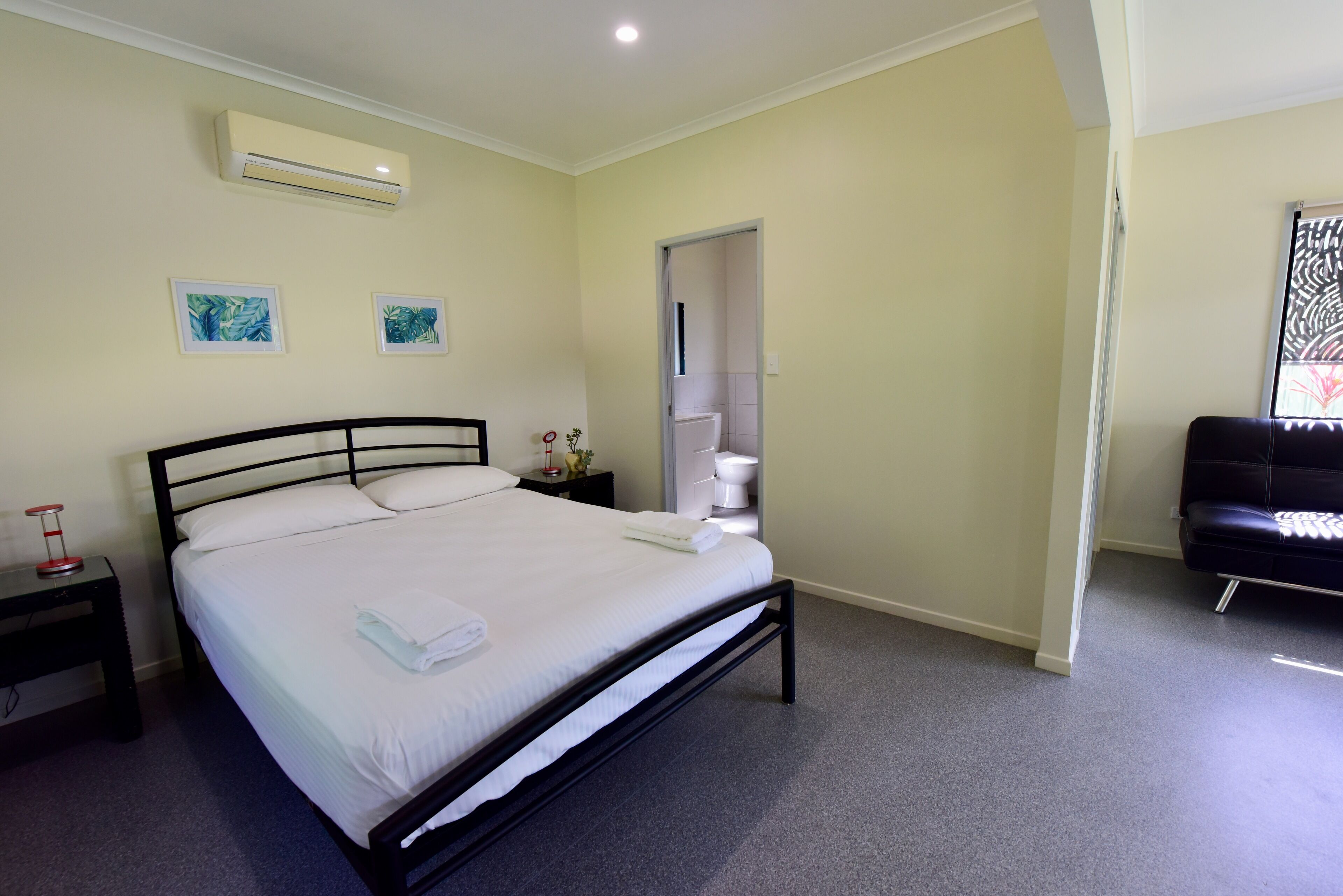 A neatly arranged bedroom with a bed, bedside table, and an air conditioning unit on the wall.