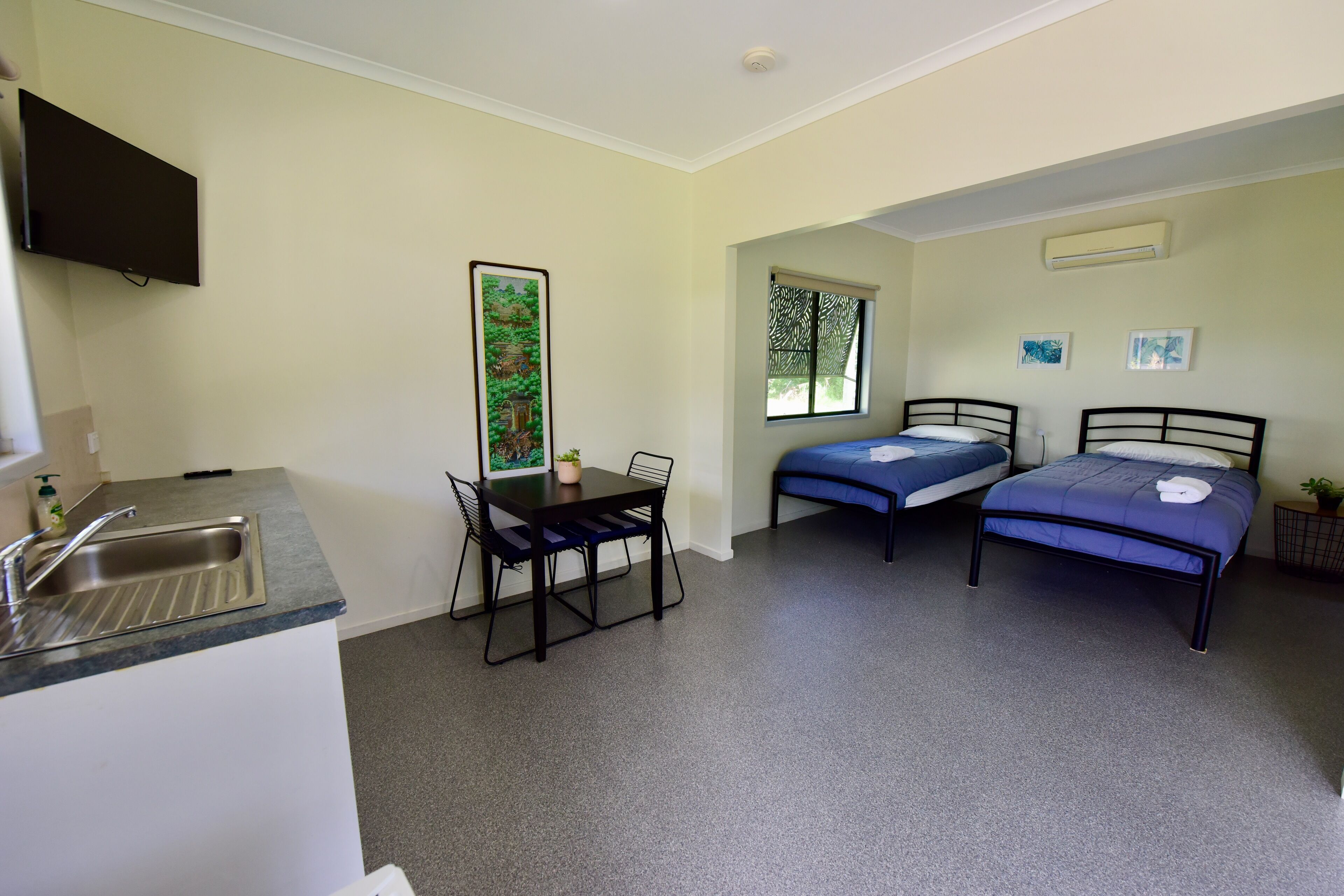 A compact room with a kitchenette, two single beds, a dining table, and a window with a view.