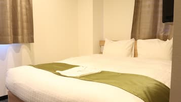 A hotel room with a bed, pillows, a blanket, and curtains.