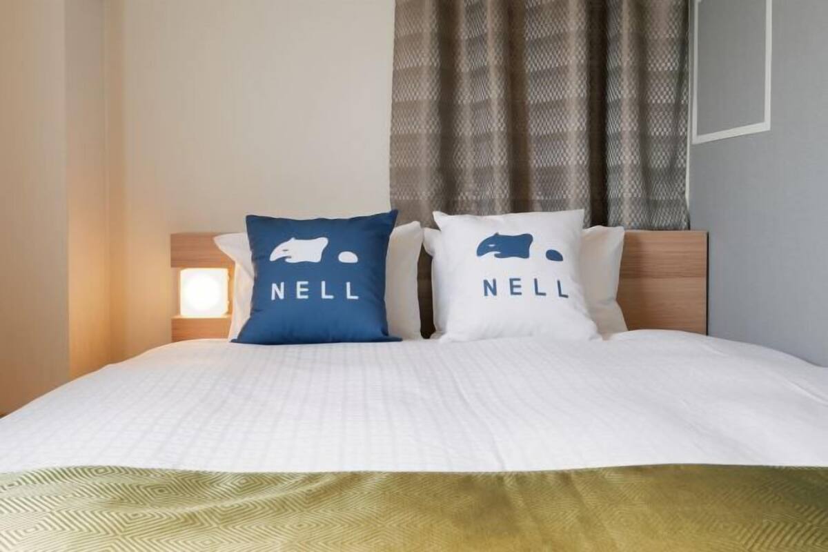 A bed with two pillows, a nightstand, and a window with curtains.