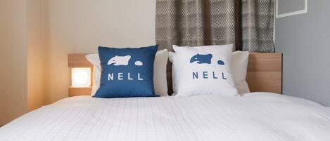 A bed with two pillows, each with a bear logo and the word 'NELL' on them.