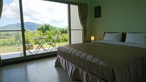 Quarto com uma cama grande, porta de vidro deslizante que dá para uma varanda com vista para vegetação e montanhas.