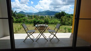 Varanda com mesa e cadeiras, vista para um jardim exuberante e montanhas ao longe.