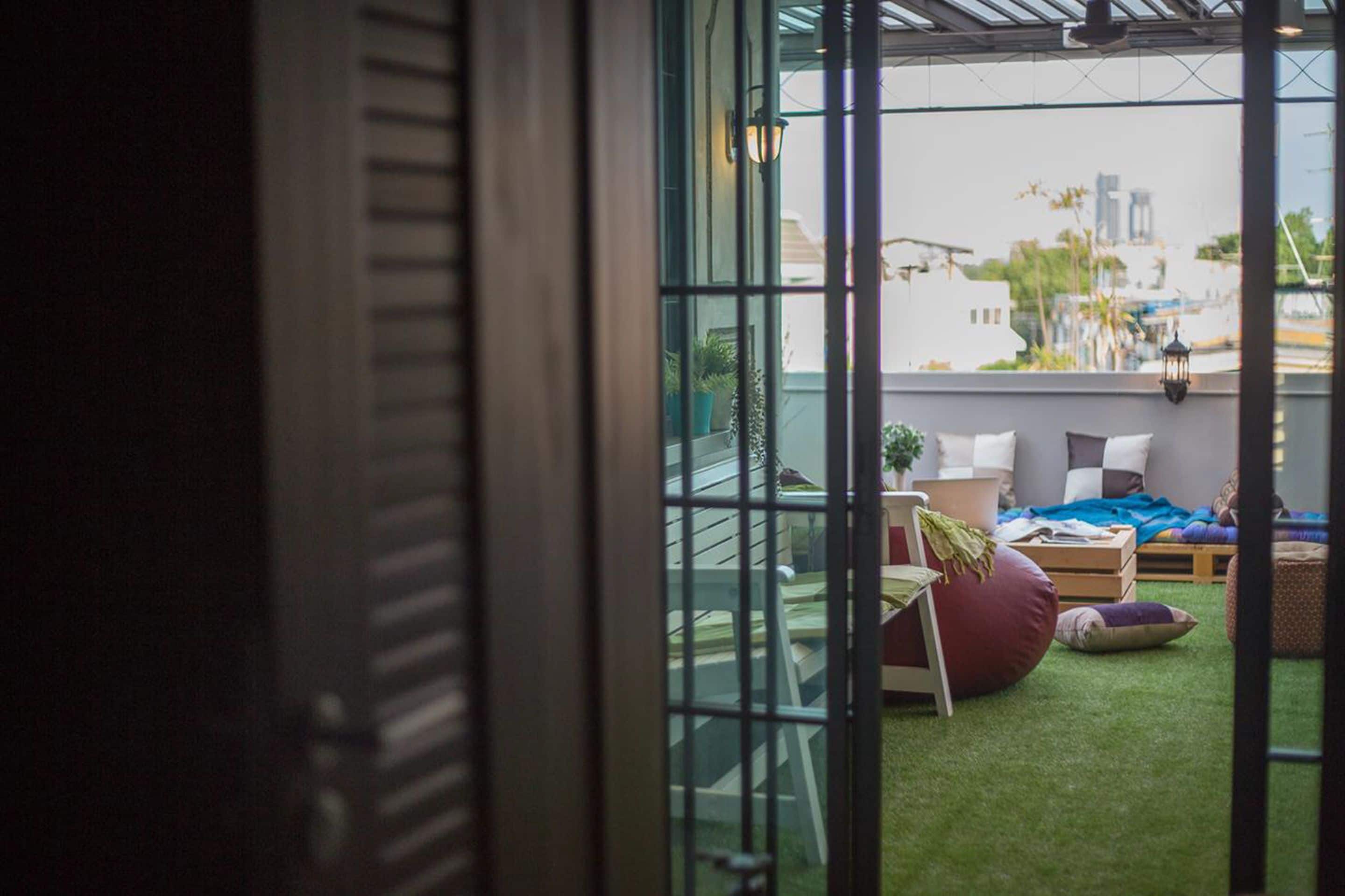 A cozy indoor space with a glass door leading to an outdoor area. Inside, there is a bed with pillows and a blanket, a bean bag chair, and a small table with a plant.