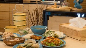 A modern kitchen with wooden cabinets, a hanging light fixture, and various dishes on the counter. - PAMA House Boutique Hostel (Bangkok)