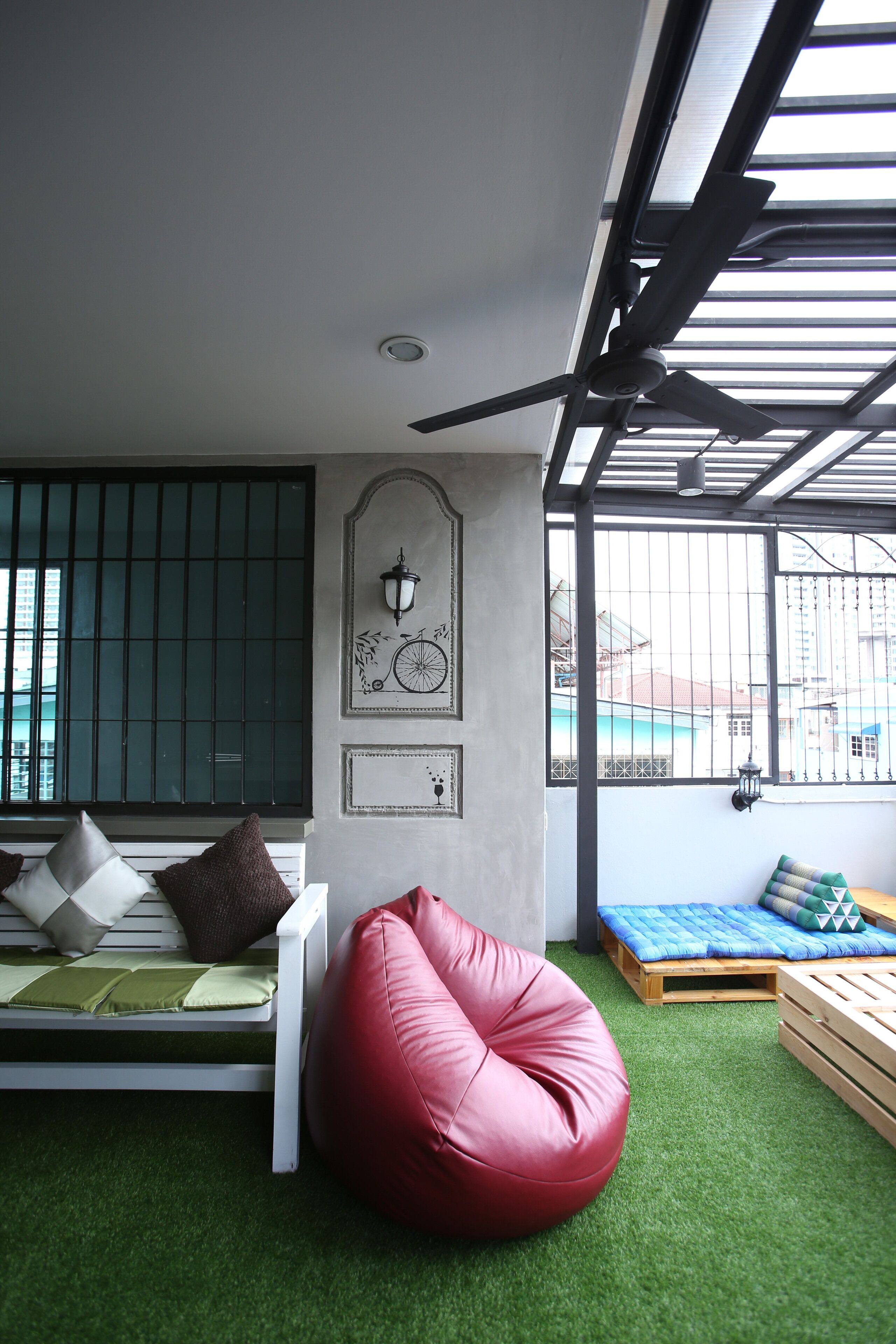 Ein Zimmer mit einem weißen Sofa, einem roten Sitzsack und einem blauen Sofa mit Kissen. Es gibt ein Fenster mit Metallgitter und einen Blick auf Gebäude im Freien.