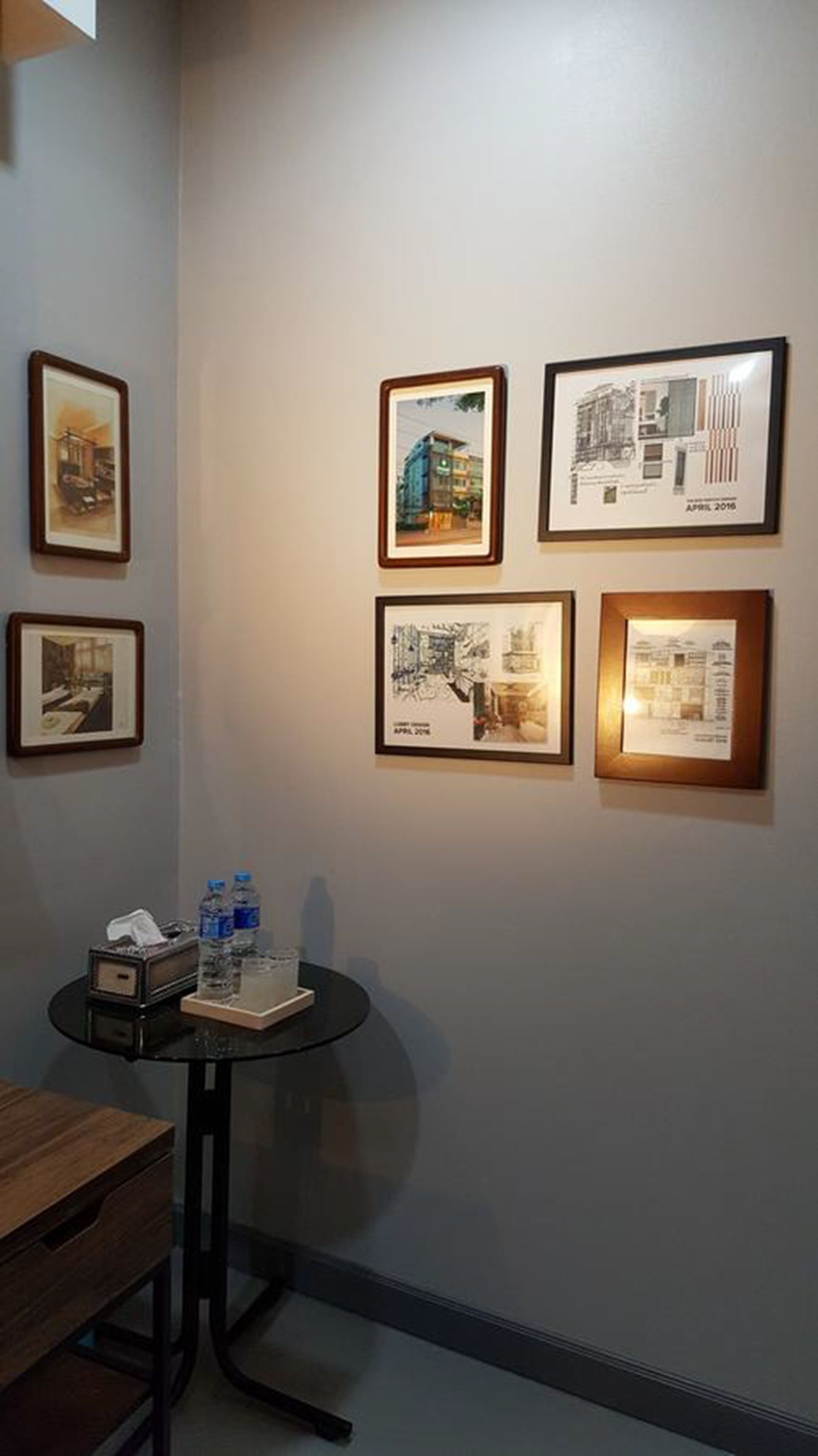 A room with a wall displaying framed architectural drawings and a small table with water bottles and a tissue box.