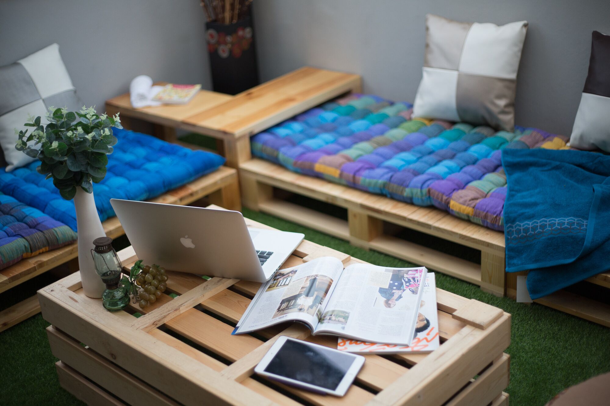 Una habitación acogedora con palets de madera como camas, una computadora portátil, un libro y un teléfono inteligente sobre una mesa de madera.