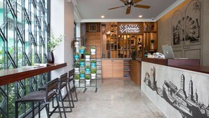 A modern cafe with a wooden counter, bar stools, and a variety of plants. - PAMA House Boutique Hostel (Bangkok)