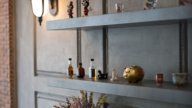 A shelf with decorative items, a vase with flowers, and a wall-mounted light fixture. - PAMA House Boutique Hostel (Bangkok)