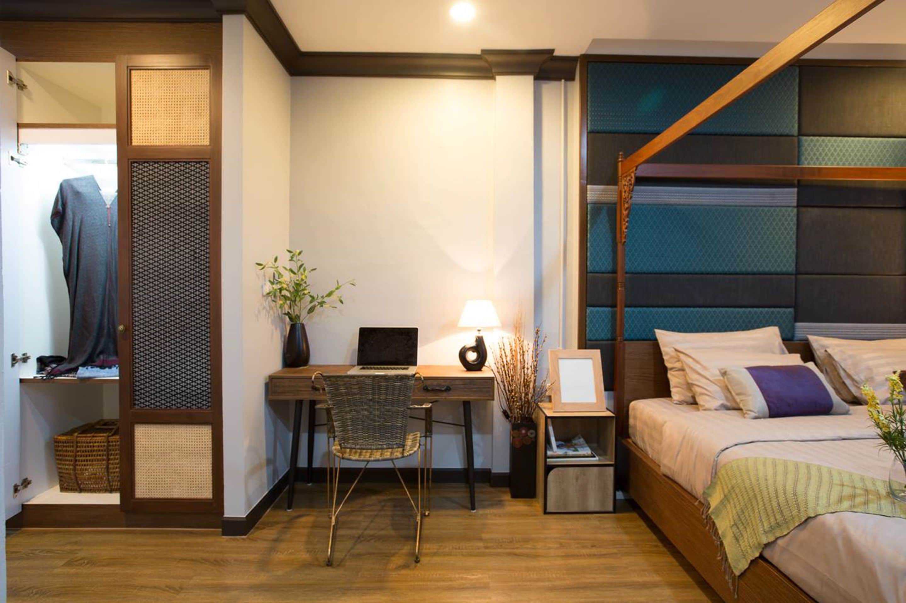 Een slaapkamer met een bed, een bureau met stoel, een laptop, een lamp en een nachtkastje met vaas.