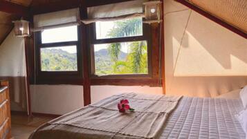 A bedroom with a bed, a window with a view of greenery, and a wooden ceiling.