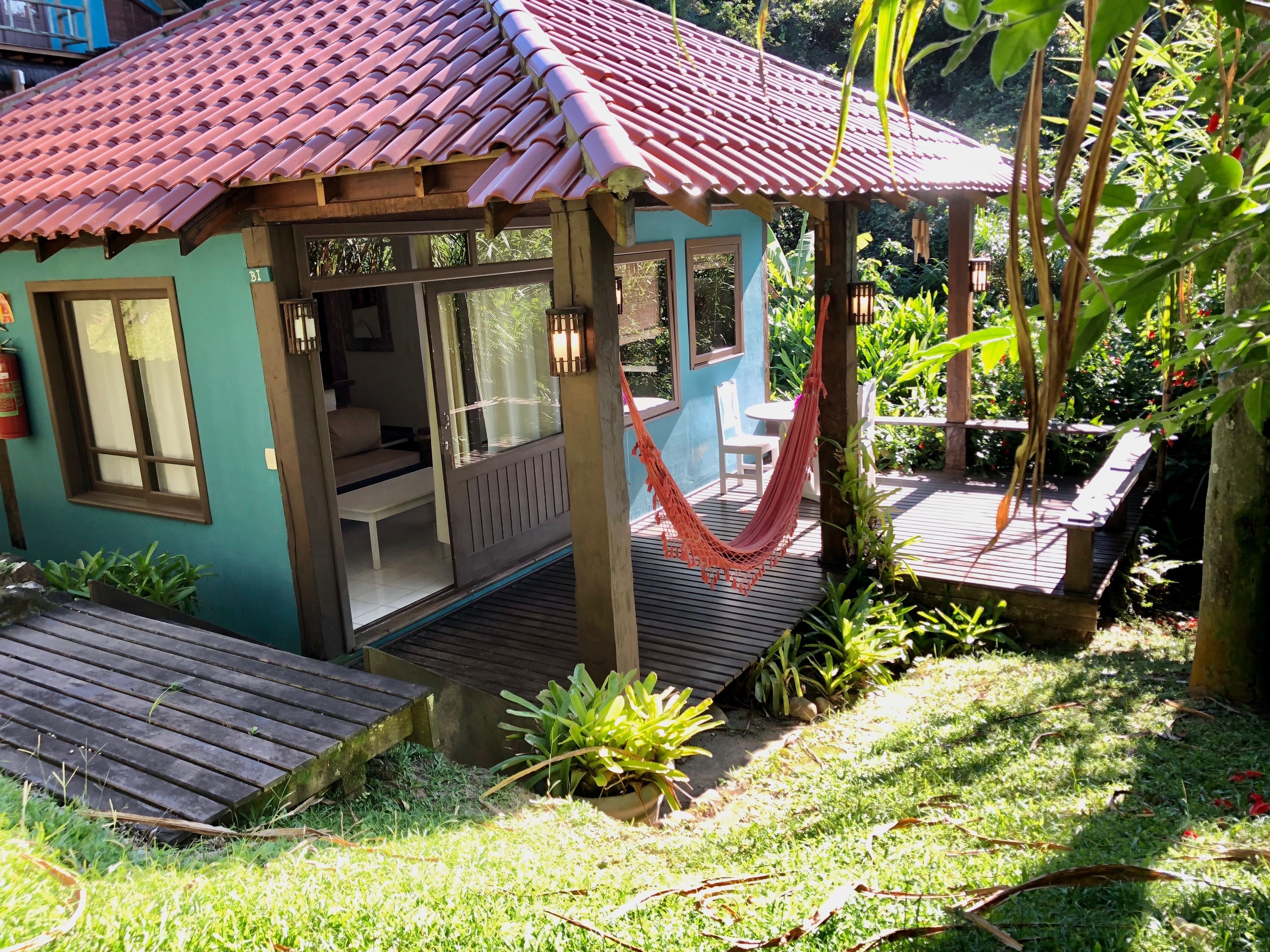 A small, single-story structure with a tiled roof, a wooden deck, and a hammock.