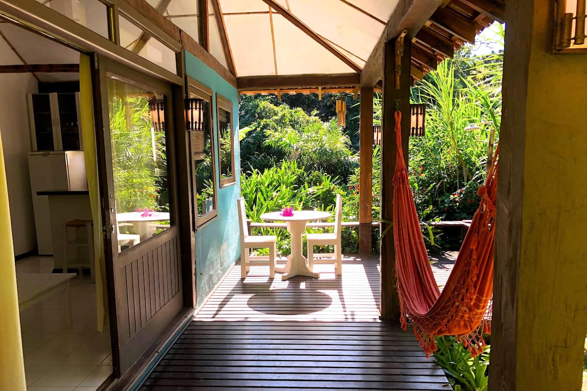 A wooden deck with a table and chairs, a hammock, and a view of lush greenery.