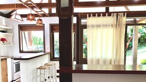 Una cocina con una isla central, taburetes blancos y vistas al exterior.