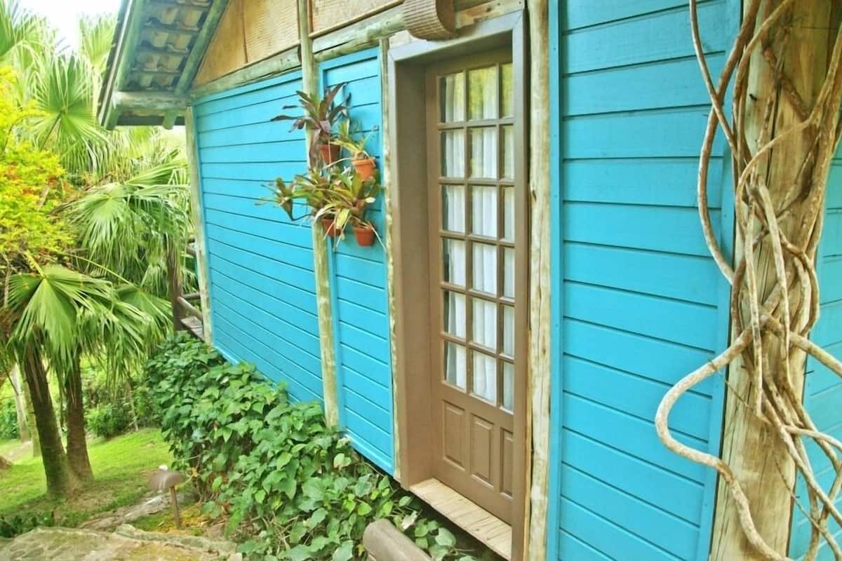 A blue house with a brown door, surrounded by greenery and a stone pathway.
