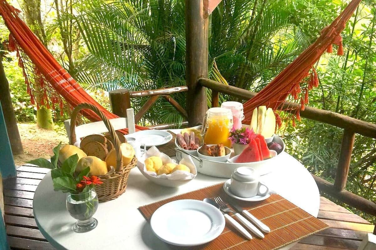 A round table with breakfast items, a hammock, and a view of a lush garden.