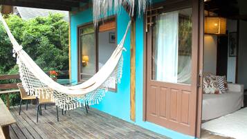 A hammock on a wooden deck, a wooden door, and a beige sofa with patterned cushions.