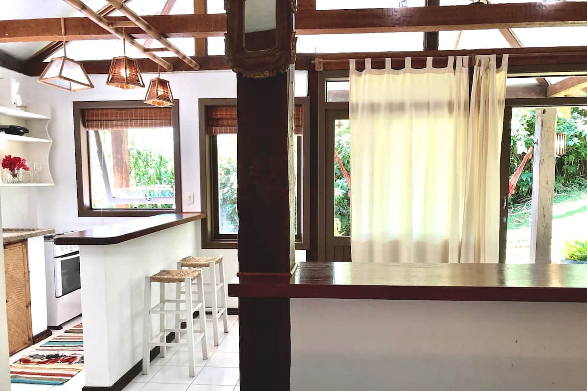 A kitchen with a white countertop, wooden stools, and a window with curtains.