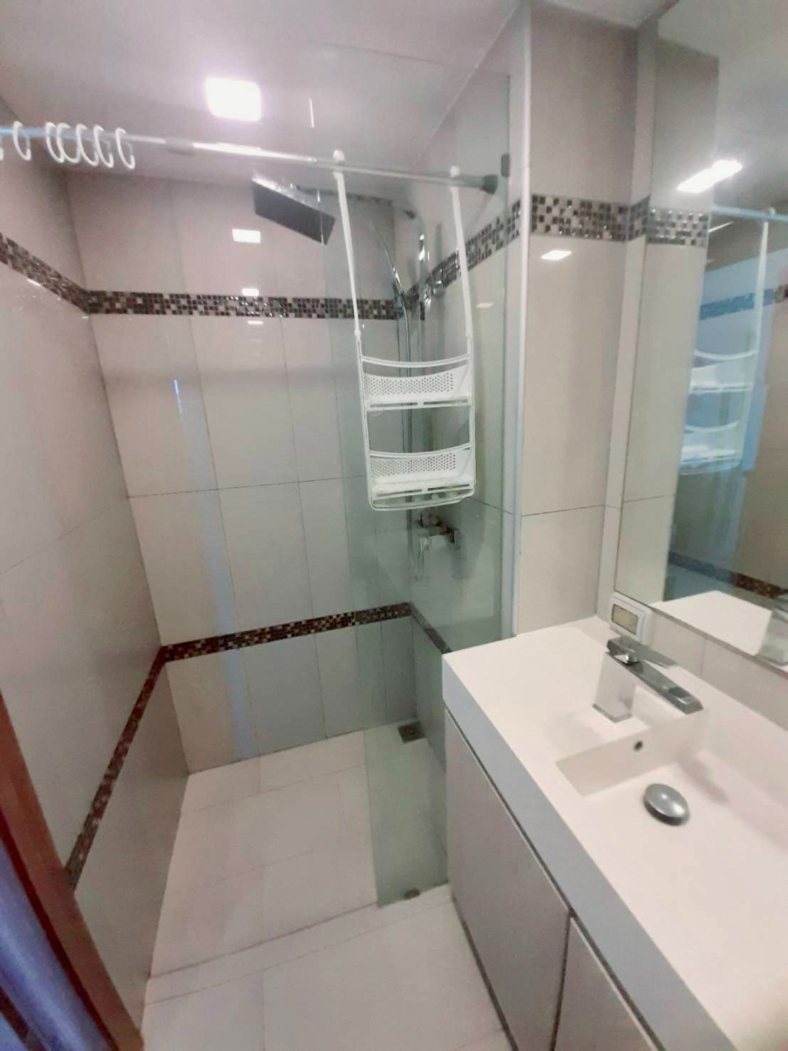 Une salle de bain moderne avec une douche à parois de verre, un lavabo blanc avec un miroir et un sol carrelé.