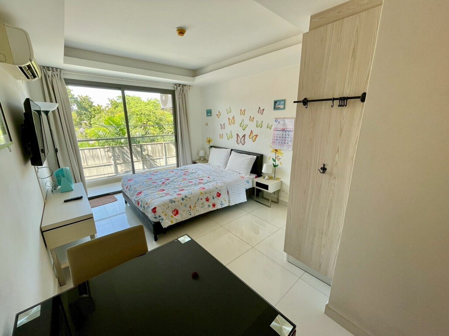 A hotel room with a bed, a desk, a chair, a TV, a window with curtains, and a calendar on the wall.