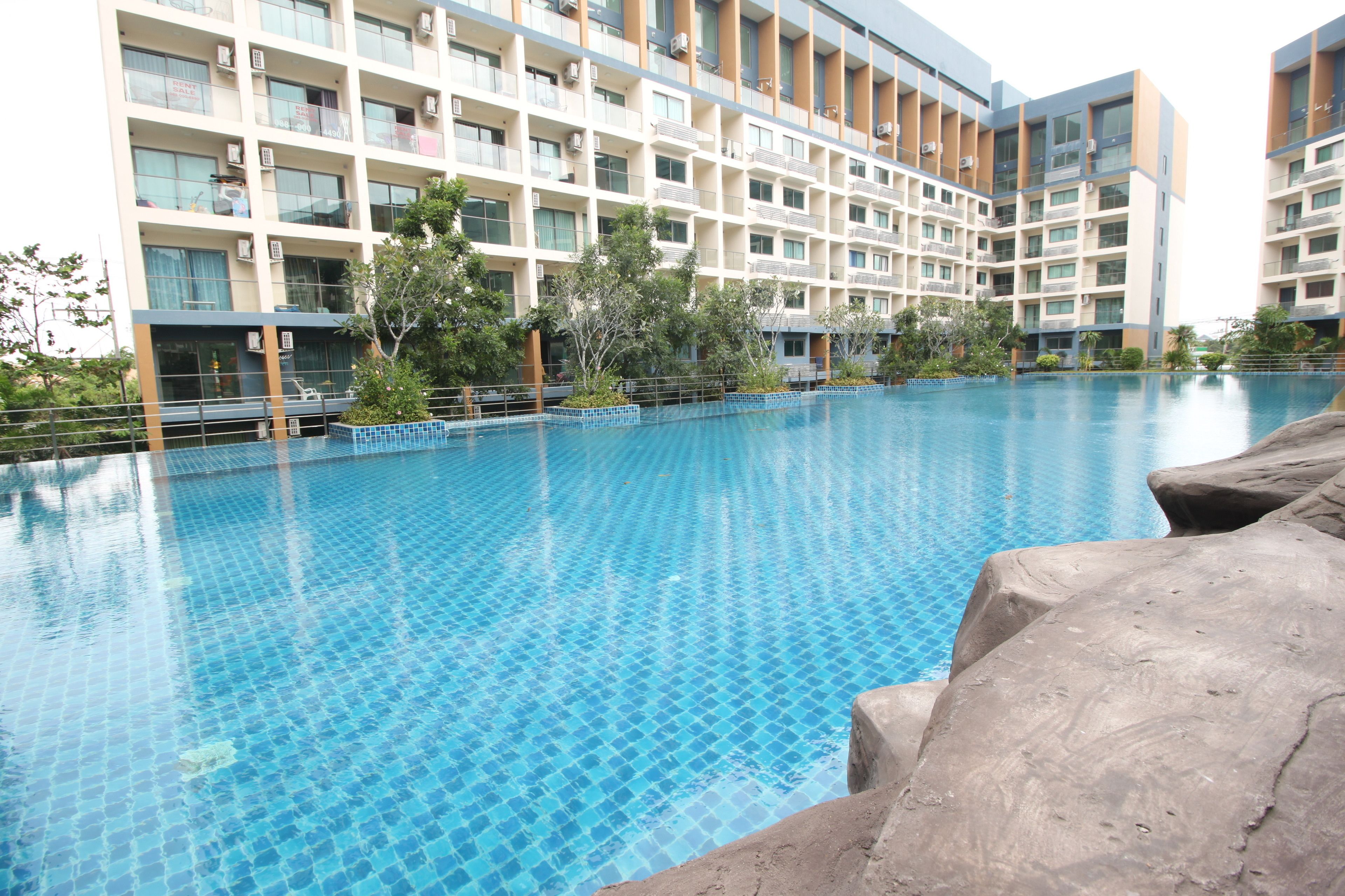 A swimming pool with tiled flooring, surrounded by a multi-story building with balconies and air conditioning units.