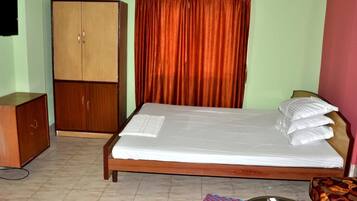 A bedroom with a bed, a wardrobe, a curtain, a bedside table, and a red mug.