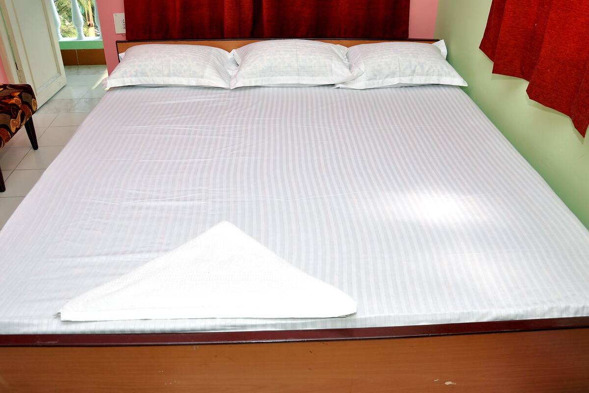 A neatly made bed with a white bedspread and pillows, a wooden headboard, and a red curtain in the background.